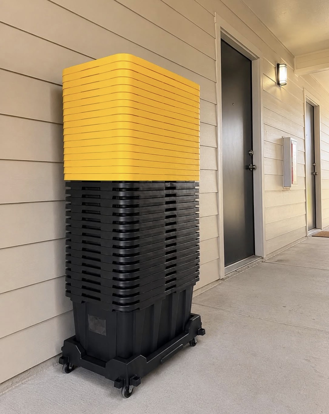 Tall stack of nested moving totes and yellow lids delivered to an apartment breezeway