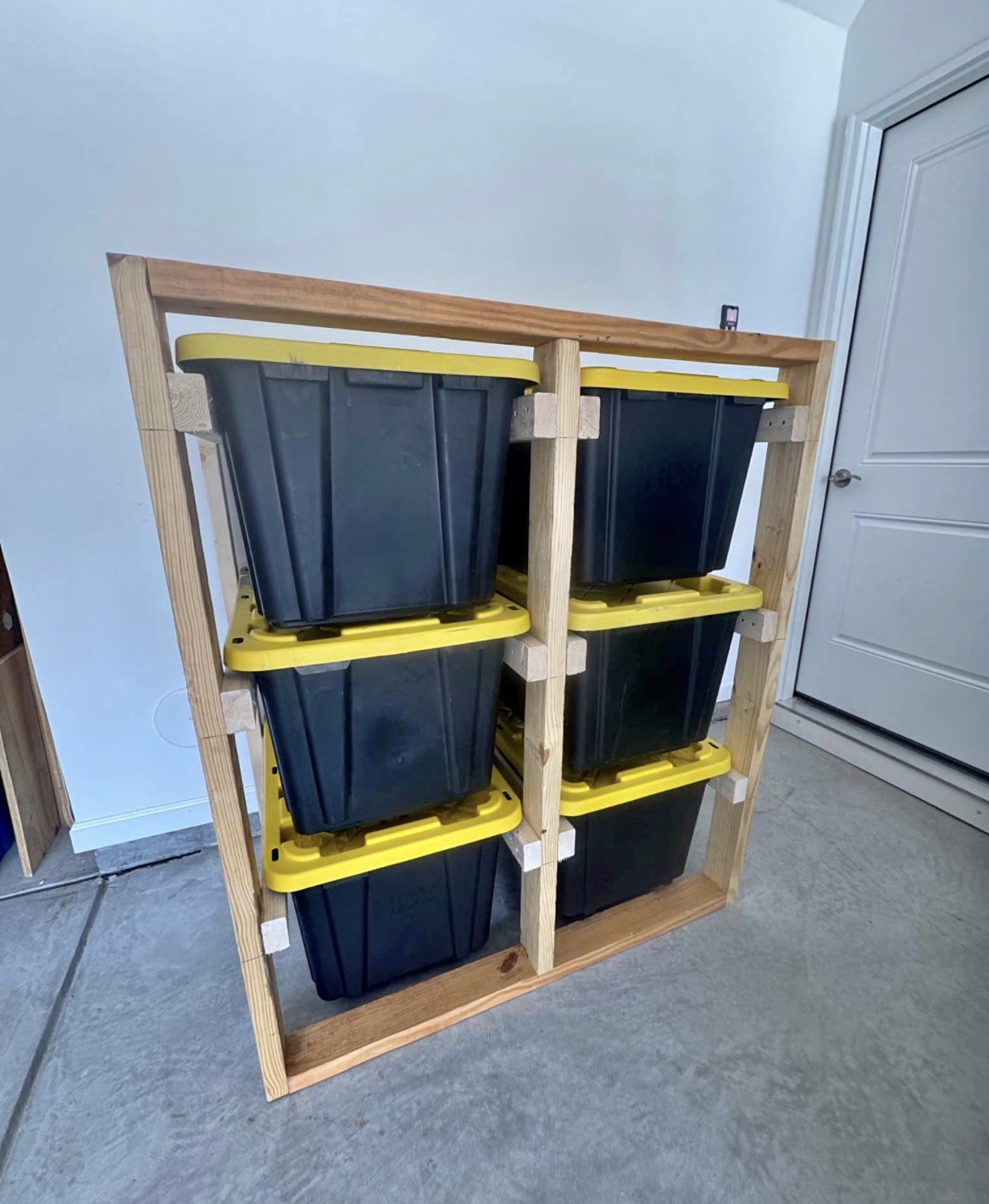 Compact six-tote storage wall with black totes and yellow lids in a small garage space